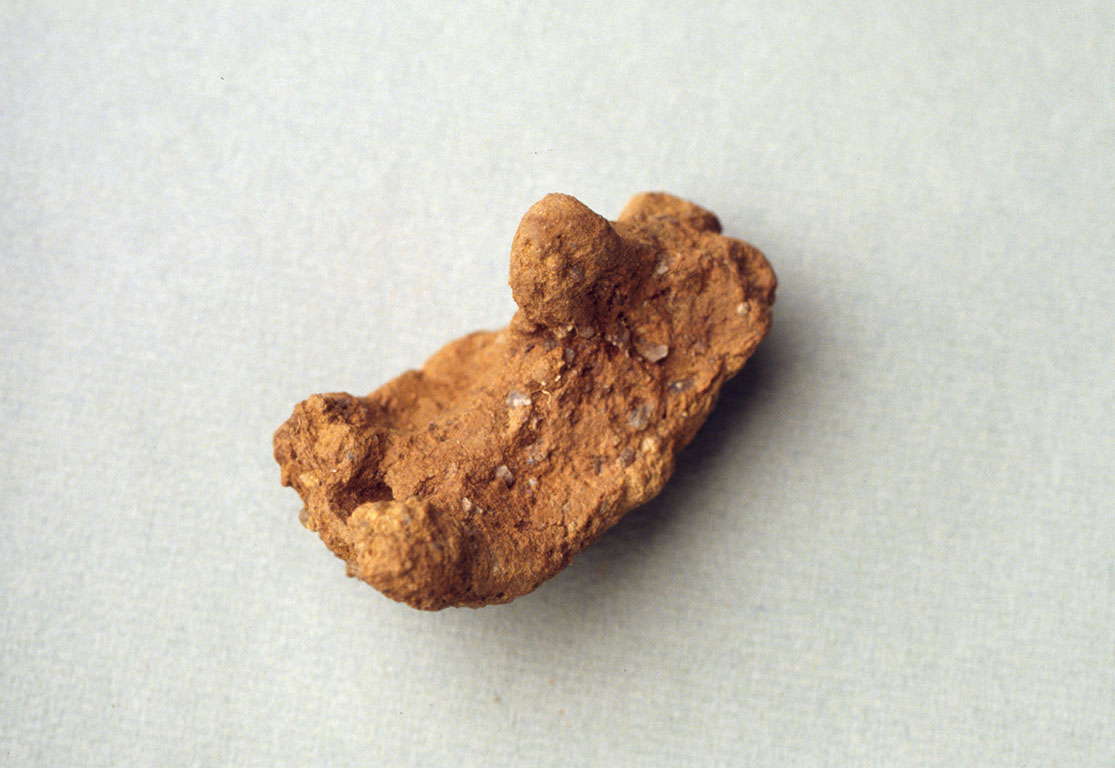 Pörrinmökistä löytynyt karhua muistuttava savi-idoli. Esine on oranssinruskea ja valkoisella taustalla. Kuva: Museovirasto.