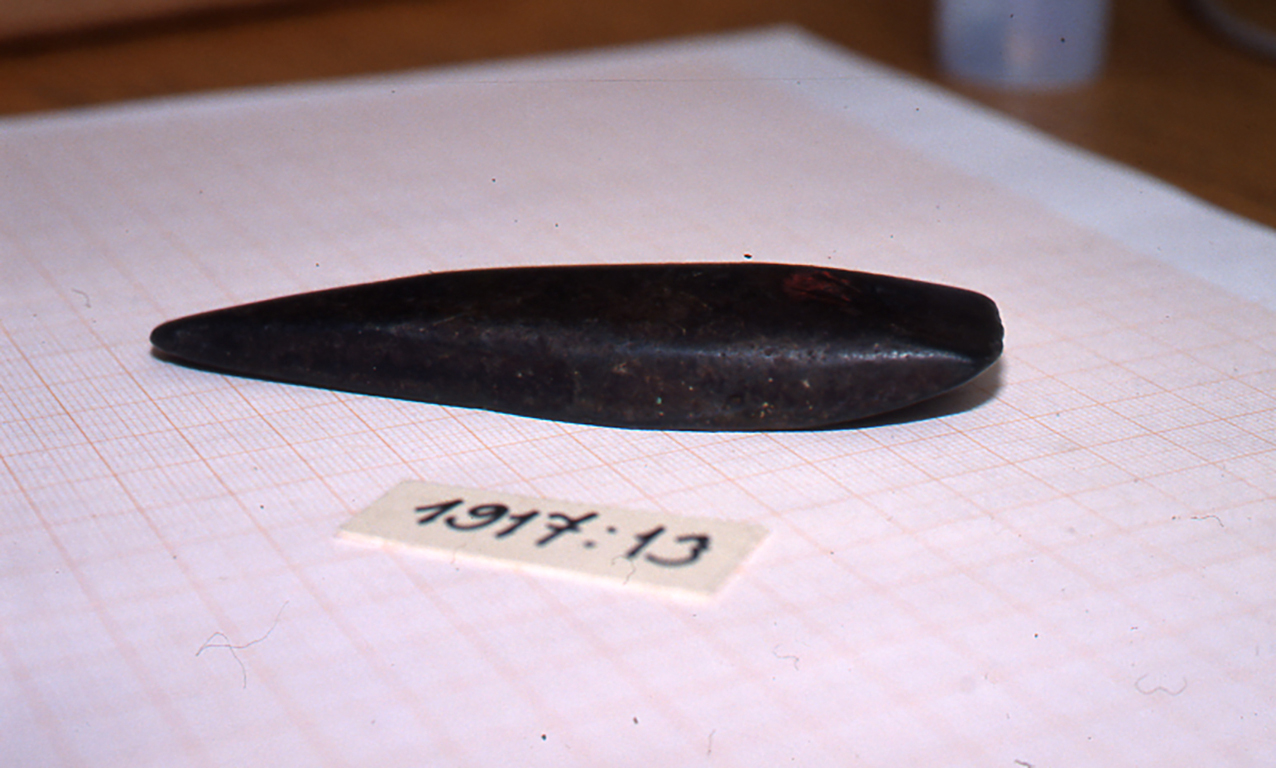 Irtolöytö Kiihtelysvaarasta. Esine on pitkulan muotoinen tumma kiviesine, jonka toinen pää on suippo ja toinen talttamainen. Esineen yhteydessä oleva numerosarja 1917:13 viittaa esineen luettelointinumeroon museoiden sähköisessä järjestelmässä.